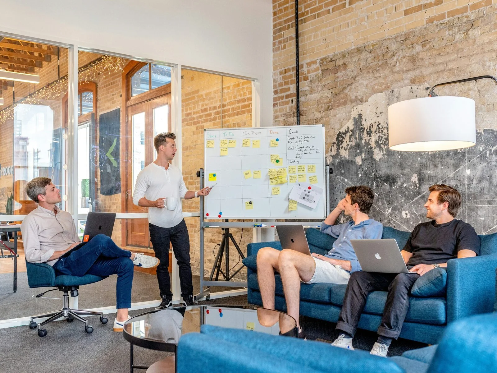 three-men-sitting-while-using-laptops-and-watching-man-beside-whiteboard-scaled-1